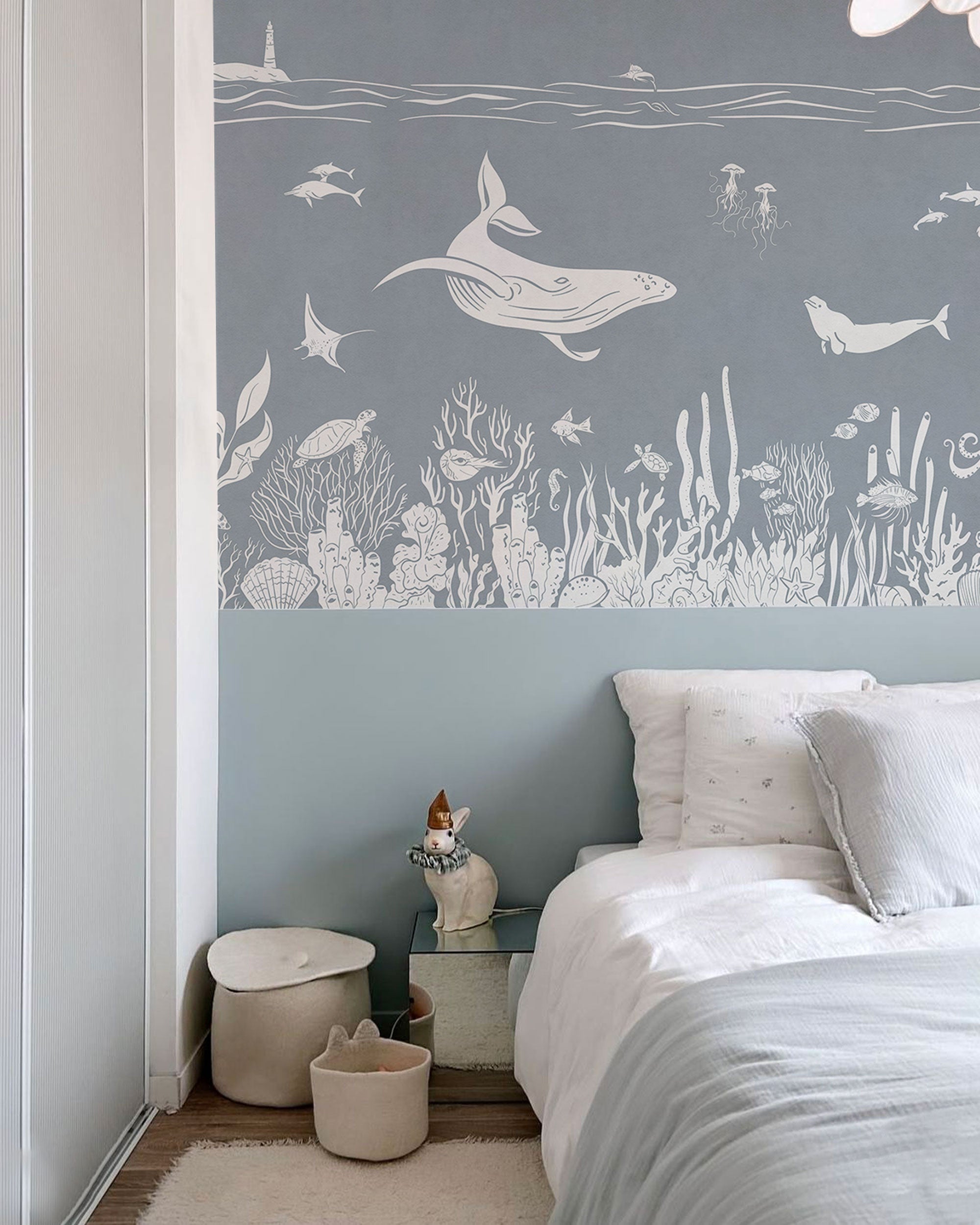 Underwater mural wallpaper in soft blue with whales, dolphins, sea life, and coral illustrations.